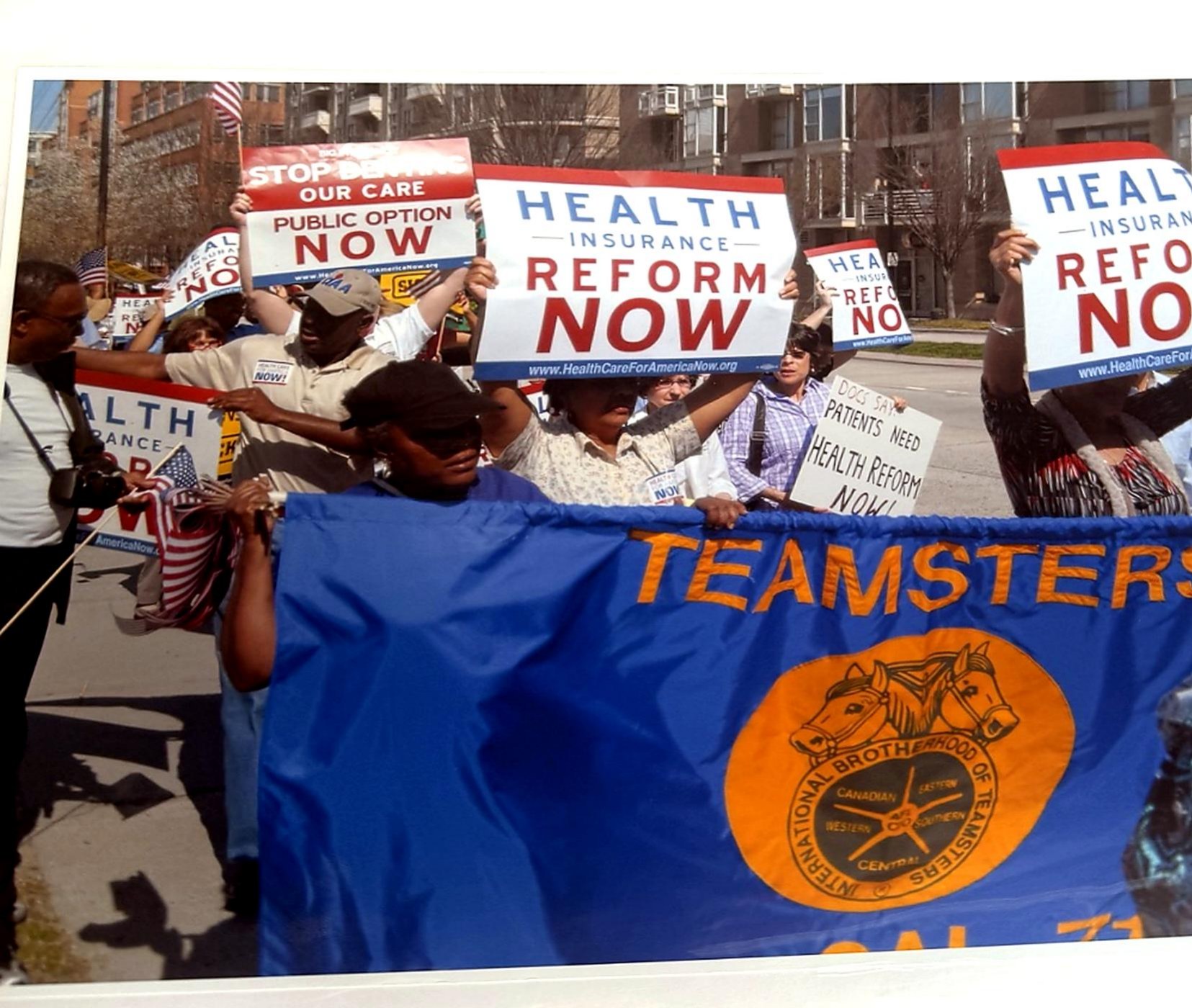 Demonstrators holding 'Health Insurance Reform Now' signs behind a large Teamsters union banner.