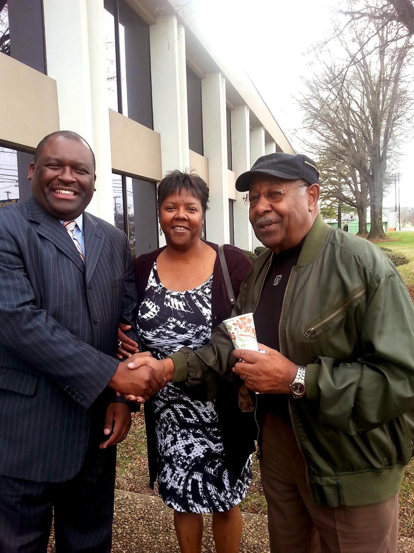 Three community members greeting one another and shaking hands outside a building.
